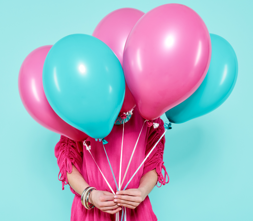 A woman wearing a pink dress holds a bunch of balloons in front of her body